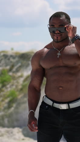 portrait of muscular black skinned man outdoors. african american sportsman without shirt wearing black sunglasses shows his trained body on camera. vertical video
