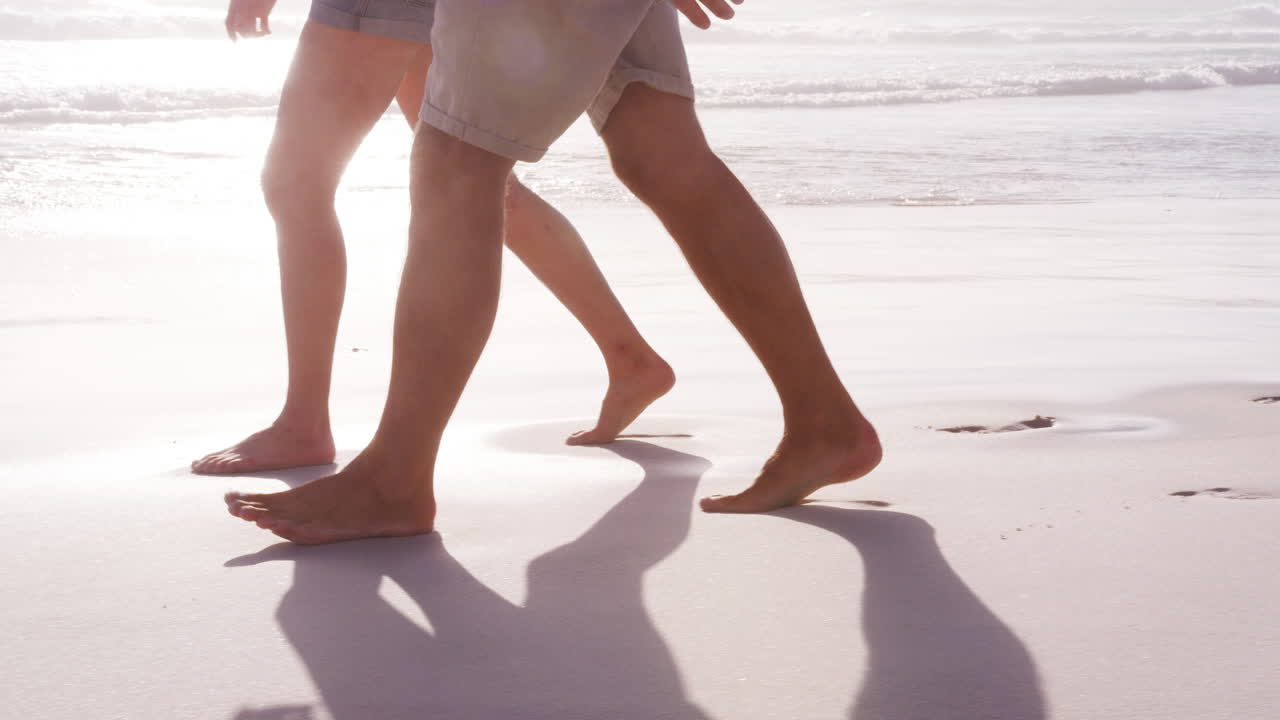 Primo piano dei piedi di una coppia in vacanza estiva che passeggia insieme lungo la spiaggia