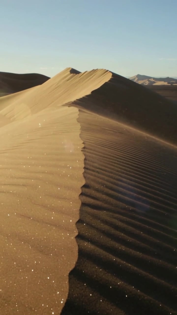 Video verticale: Telecamera che si allontana panoramando la cresta di una duna tra le dune, mostrando increspature e granelli scintillanti