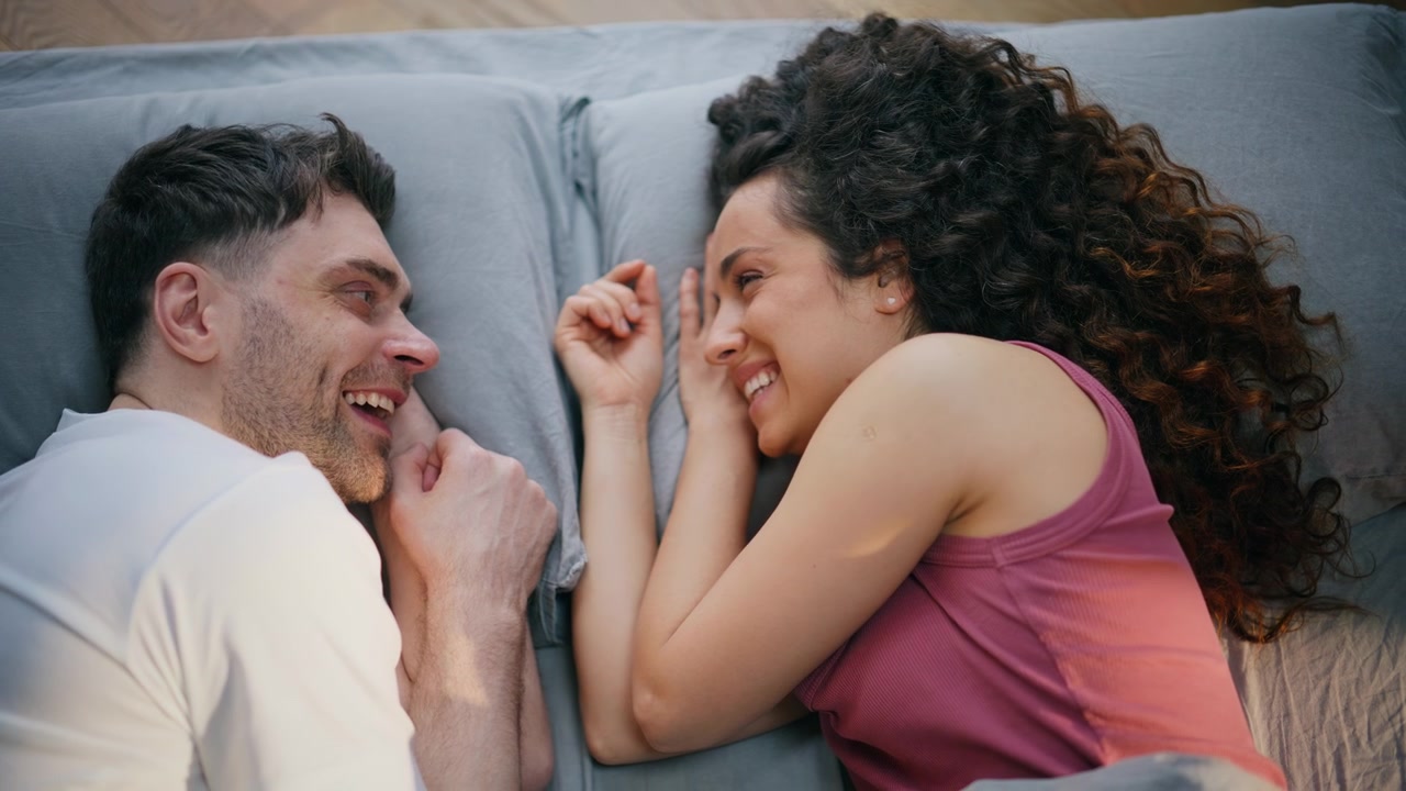 Couple lying face to face laughing bed together. Playful morning closeup home.