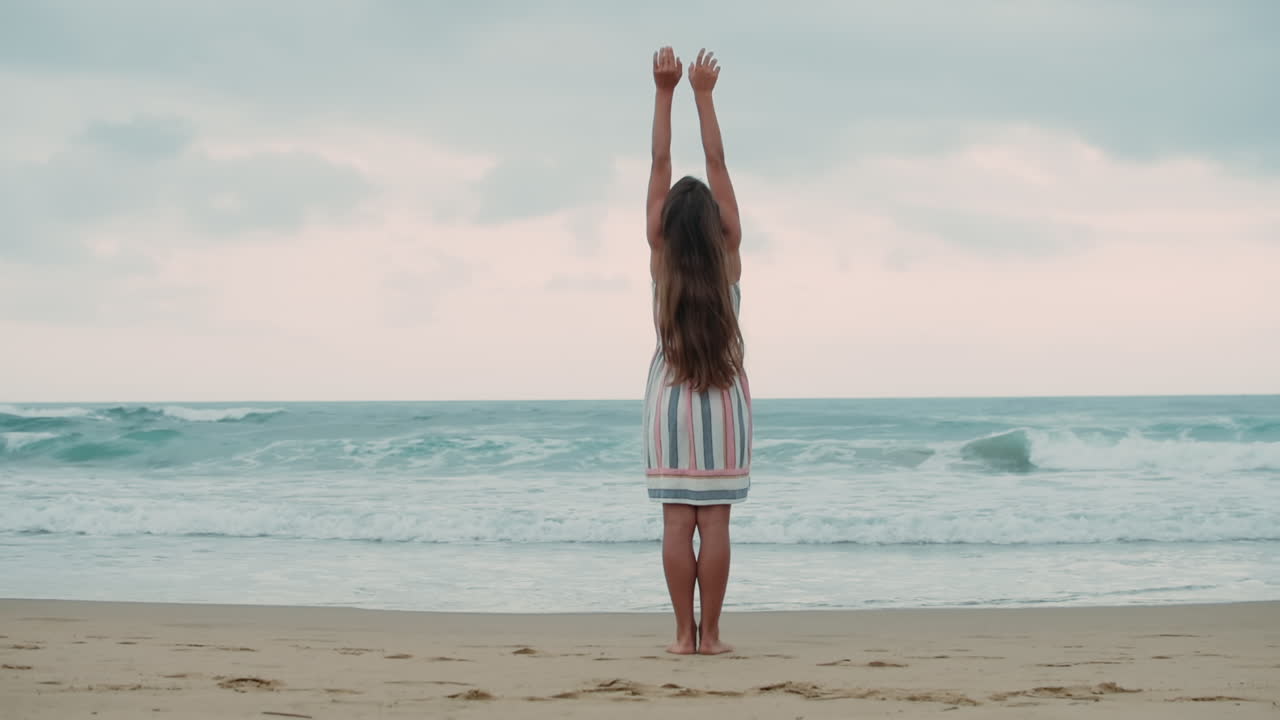 mujer joven levantando el brazo en la orilla del mar. niña despreocupada disfrutando del amanecer en la playa.
