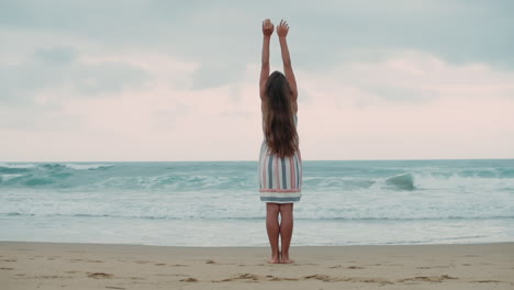 young woman raising arm at seaside. carefree girl enjoying sunrise at beach.