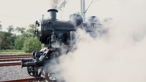 a departing steam historical train disappears into the distance and a thick cloud of white steam