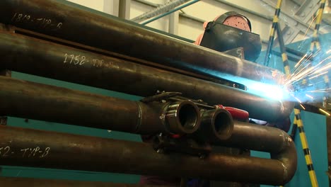 reverse zooming in shot of a welder welding big pipes in a factory with intense light and sparks emitting from the operation