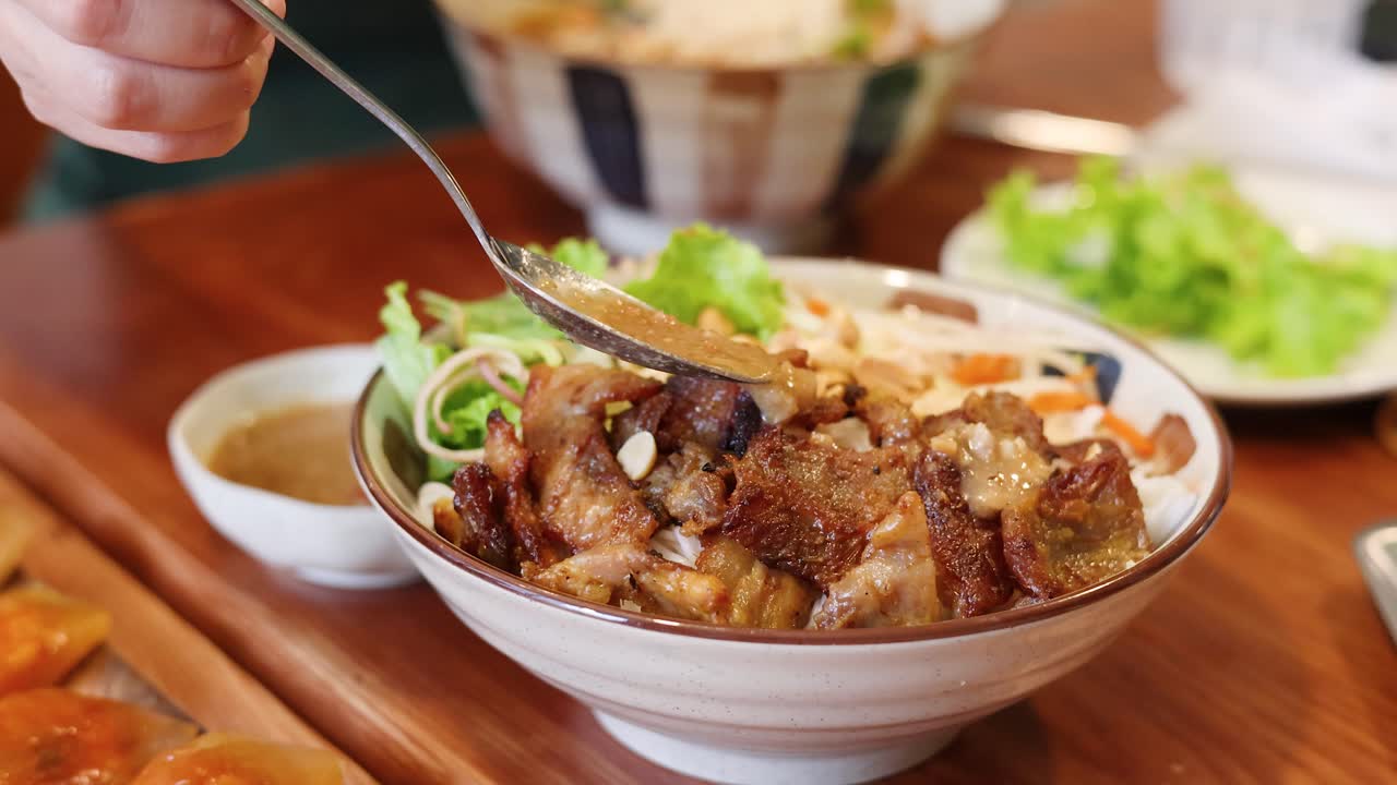 Rekaman jarak dekat sendok menuangkan saus gurih di atas daging babi panggang dan bihun.