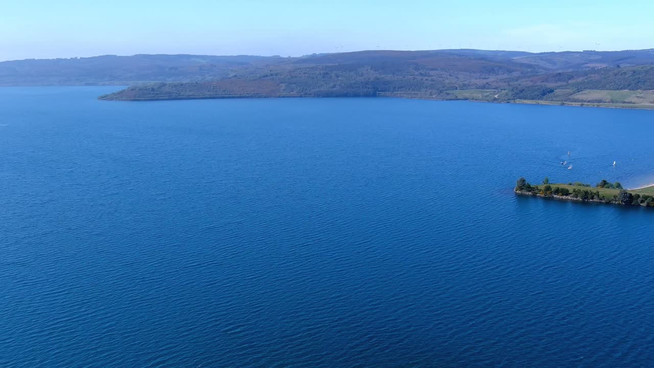 vista aérea desde un dron sobre el lago con bosques a los lados, su zona de playa y jardín, pequeños veleros practicando