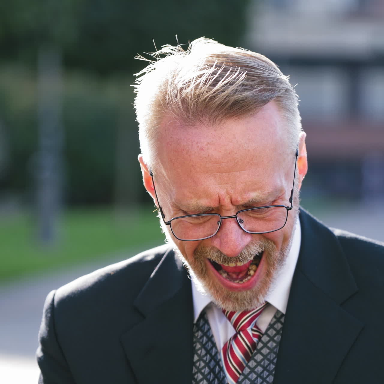 Portrait of sad businessman in glasses outdoors. Mature man in tie and suit is upset about something while sitting with his phone in the street.