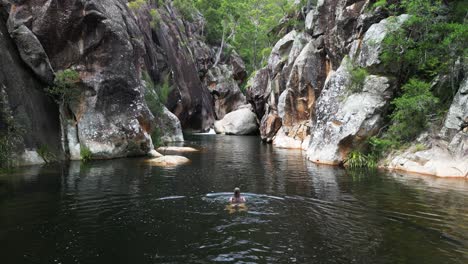 una turista femenina nada en un aislado pozo de agua australiano rodeado de altas paredes de arenisca de colores