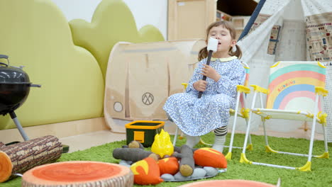 one girl toddler playing camping game at home, pretends roasting marshmallow on bonfire and eating it