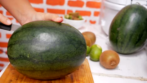 cortando la sandía por la mitad en la tabla de cortar en la cocina.