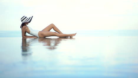 High-key-ethereal-shot-of-beautiful-Asian-woman-with-big-hat-lying-on-edge-of-pool