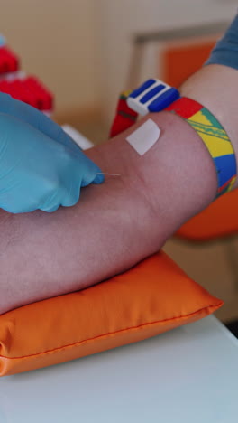 female hands in blue gloves taking a blood sample for tests. hand of doctor injects a syringe into a vein of a male patient. close-up vertical video