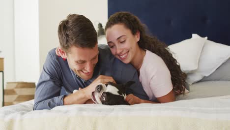 Caucasian-couple-playing-with-dog-in-bad-at-home