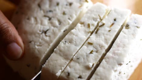 close-up of a hand slicing fresh paneer cheese on a wooden cutting board