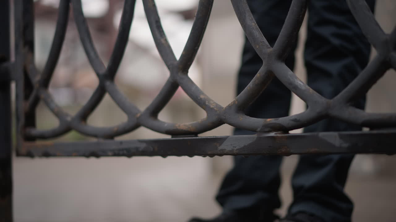 Ringhiera di ferro bagnata, piedi di donna che scendono dalla ringhiera su un marciapiede con pozzanghere, primo piano di scarpe e jeans, gocce di pioggia su metallo arrugginito, atmosfera urbana nuvolosa, movimento incerto e solitudine.