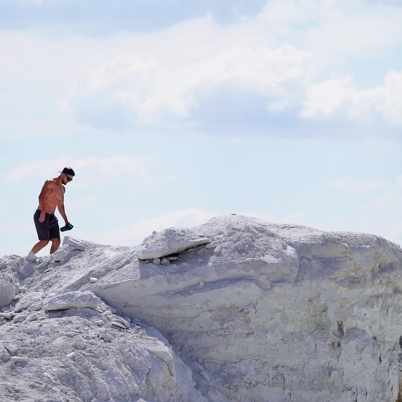 Slow motion of strong athlete in the mountains. Shirtless sportsman walking up the white hill in summer. Muscular man exercises outdoors.
