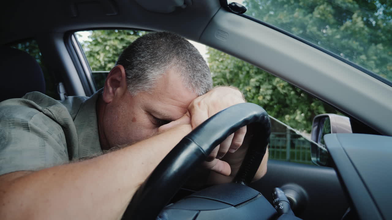 피곤한 중년 남자가 자동차 바퀴에 머리를 얹었다
