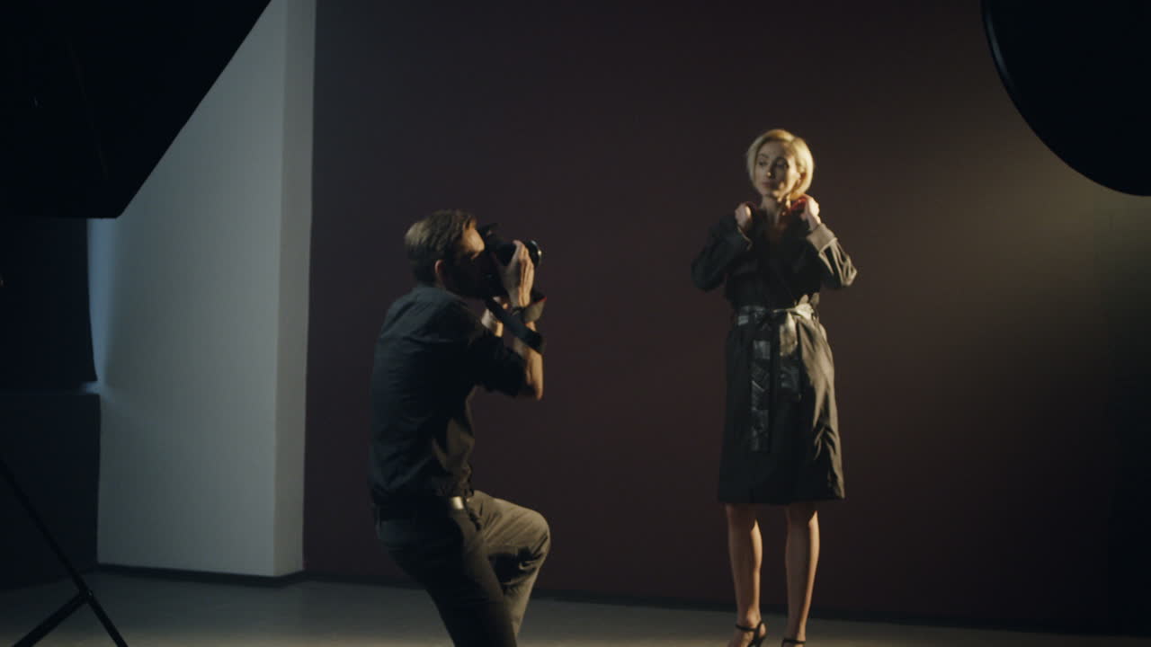 사진 작가가 그녀의 사진을 찍는 동안 어두운 스튜디오에서 포즈를 취하는 백인 젊은 여성 모델