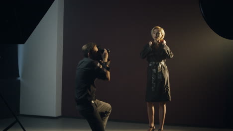 Caucasian-young-female-model-posing-in-the-dark-studio-while-the-photographer-taking-shots-of-her