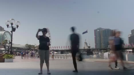 Time-lapse-in-Darling-Harbour,-Sydney-Australia-with-people-flowing-and-a-ferris-wheel-in-the-background