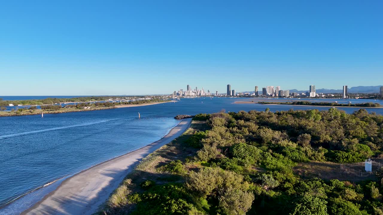 Drone footage captures the serene Gold Coast Seaway with lush greenery and calm waters under clear skies during sunset