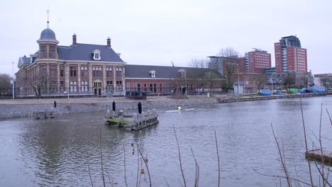 two rowers rowing along utrecht's canal on a cloudy day in the netherlands, with a traditional brick building in the background