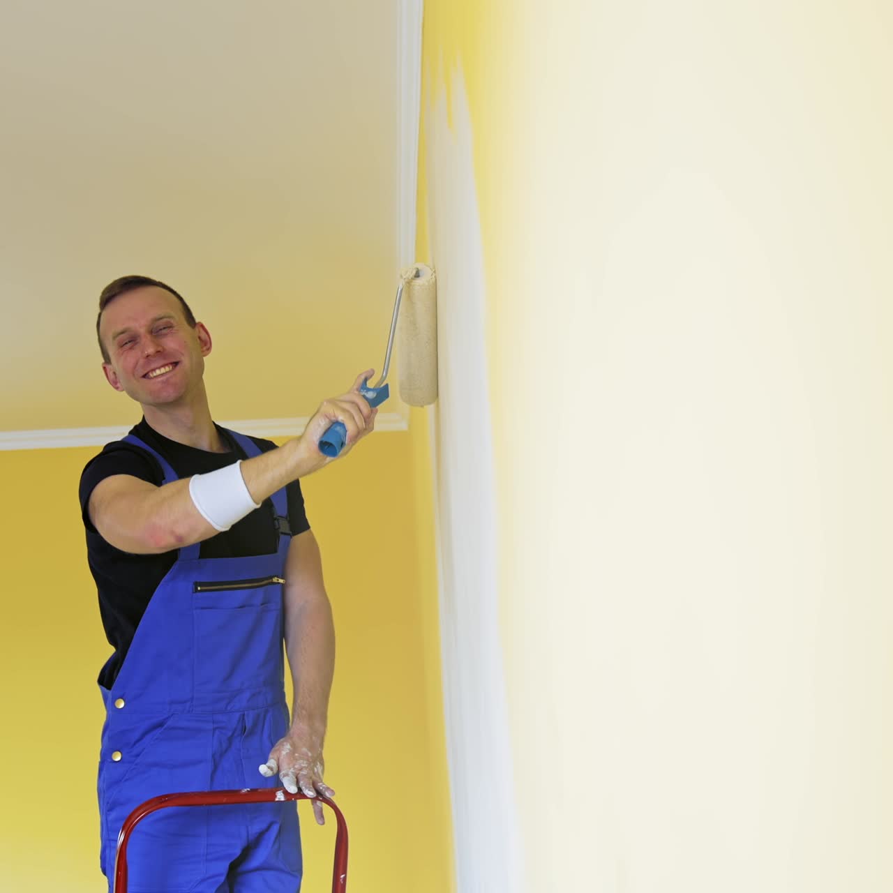Man in work overalls paints the wall. Workman in the uniforms painting the walls with paint roller