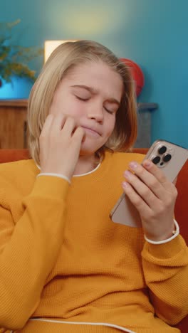 teenager boy checking smartphone looks sad receives bad news negative test results sitting on sofa