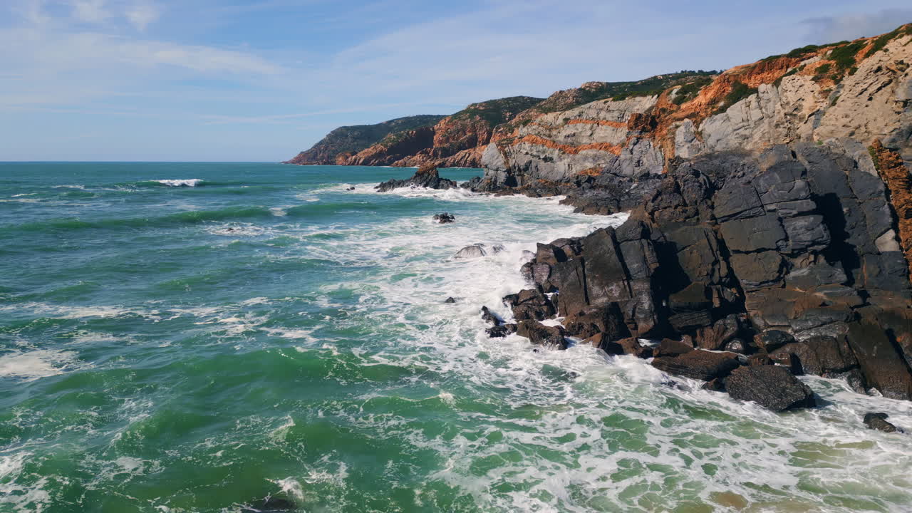 Ocean surf splashing coastal rugged cliffs with foam. Aerial stormy sea waves.
