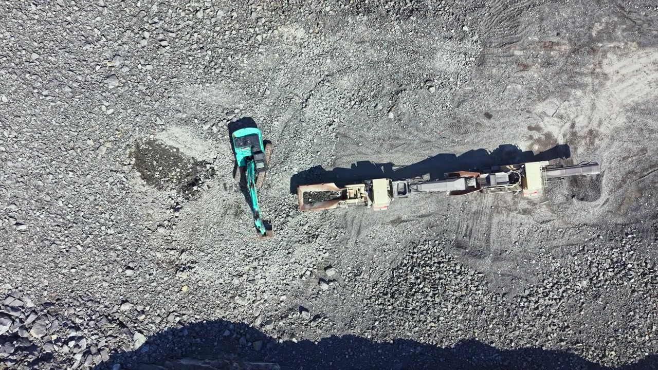 Granite quarry site showing an excavator and a truck preparing stone material for transportation