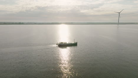 Aerial dolly out shot of the Dutch boat Luxe Motor crossing the calm sea with a wind turbines in the background. in Holland
