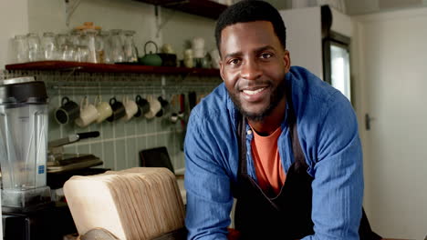 a young african american male barista smiles warmly, leaning on a cafe counter