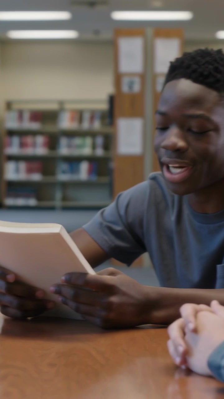 Vertical video: Placing paperback, woman causing teen in gray tee grabbing and reading at library