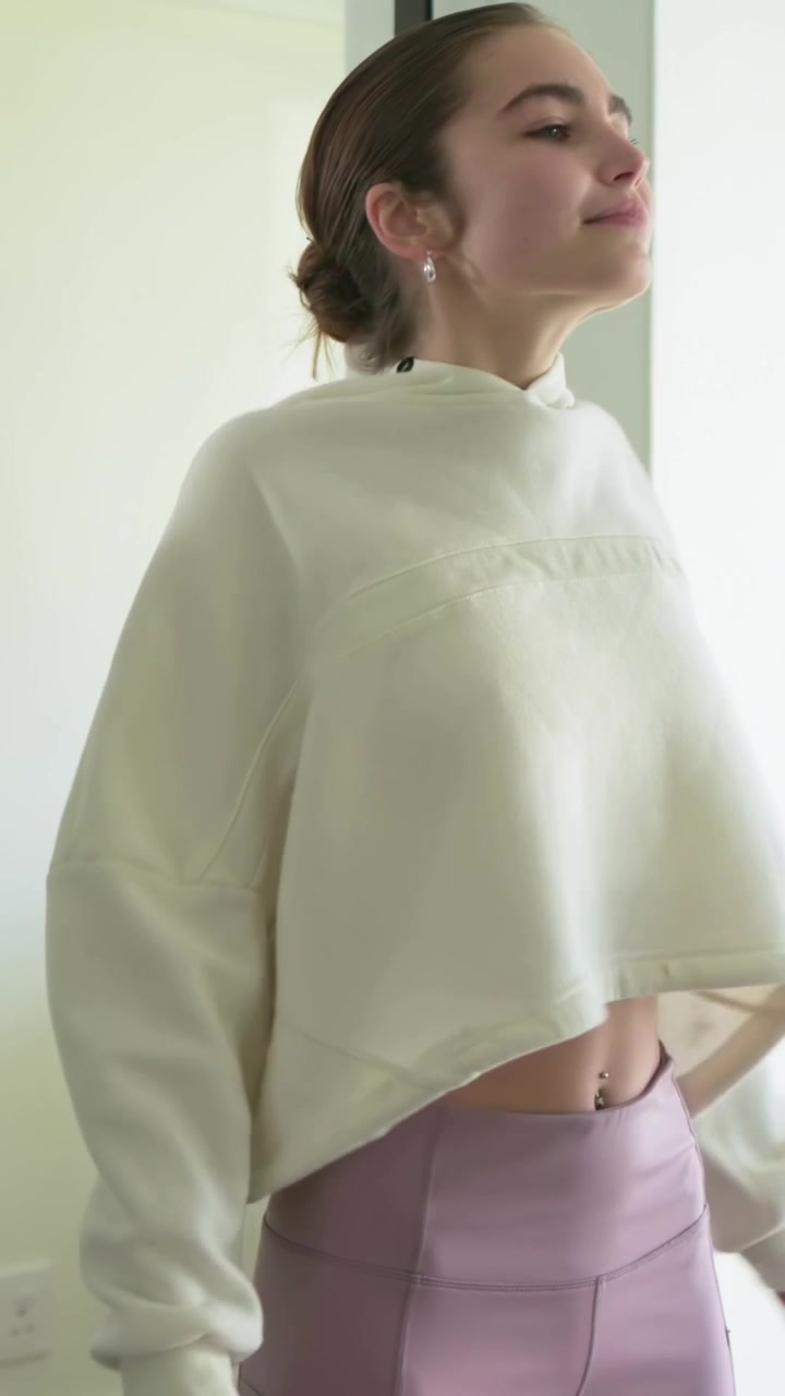 Vertical video: Entering right, woman in cream hoodie doing neck rolls, warming up at home, bike