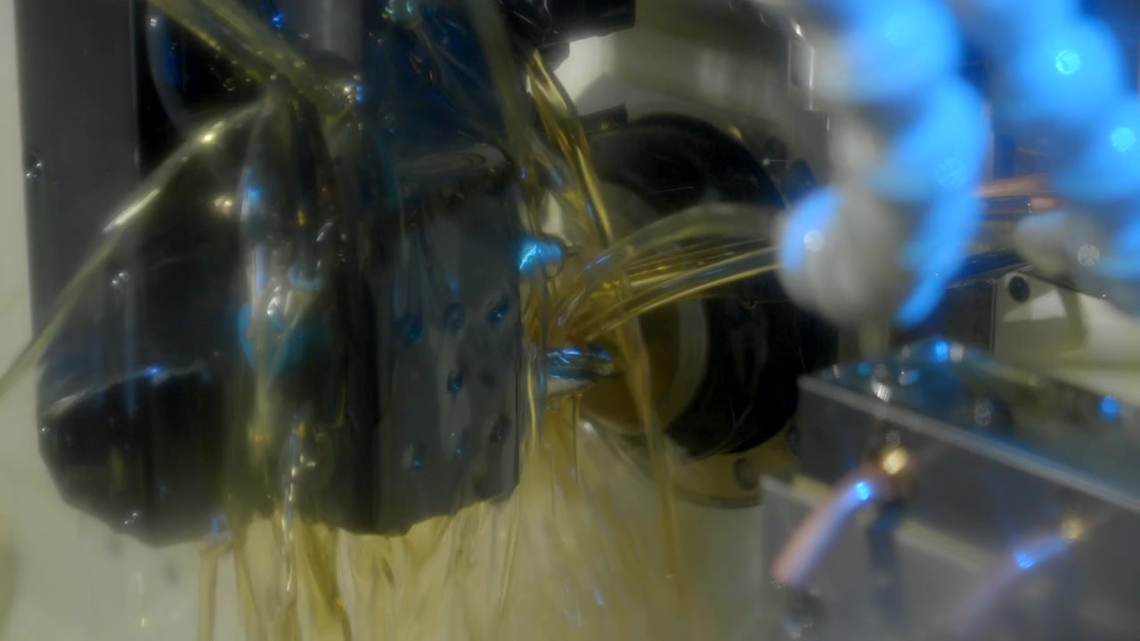 Close-up of a CNC machine operating under heavy coolant flow while machining a metal component in cinematic blue lighting.
