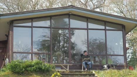 young man relaxing under cabin porch in woods