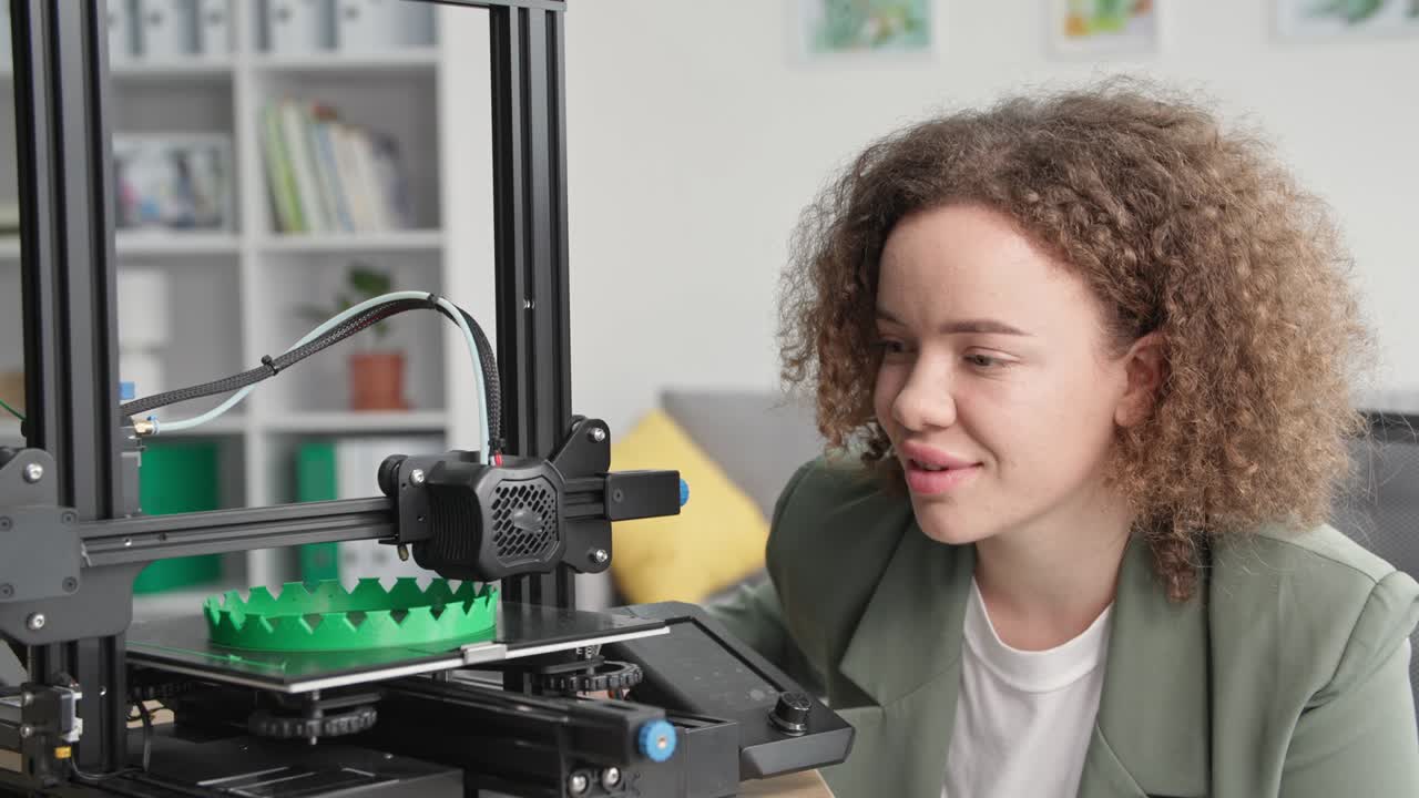 retrato de una joven y hermosa diseñadora observa las tecnologías modernas y mira la impresión de trabajo en una impresora 3d