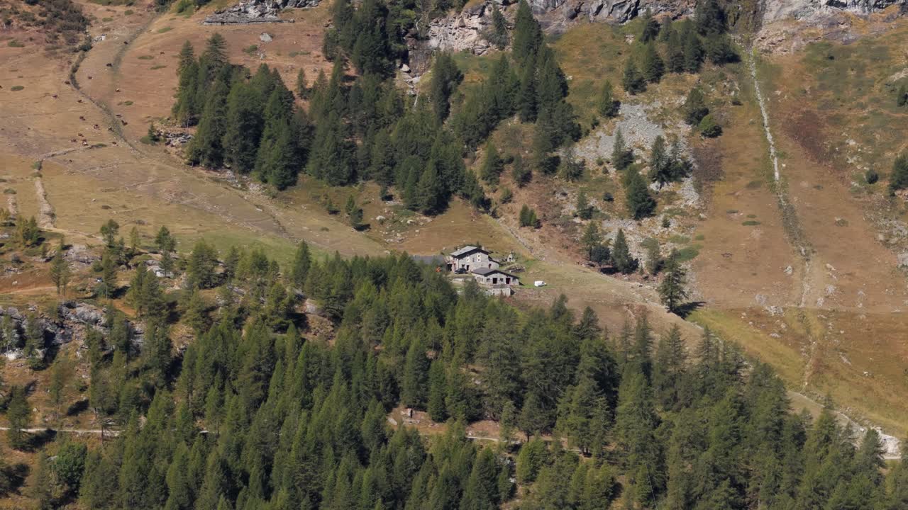 Aerial panning right of an isolated rock cabin in a mountain pine forest in Italy, Aosta Valley, Valle d’Aosta, surrounded by alpine nature