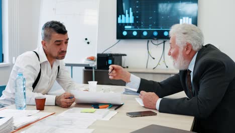 two business person discussing market analysis sitting at desk in meeting.