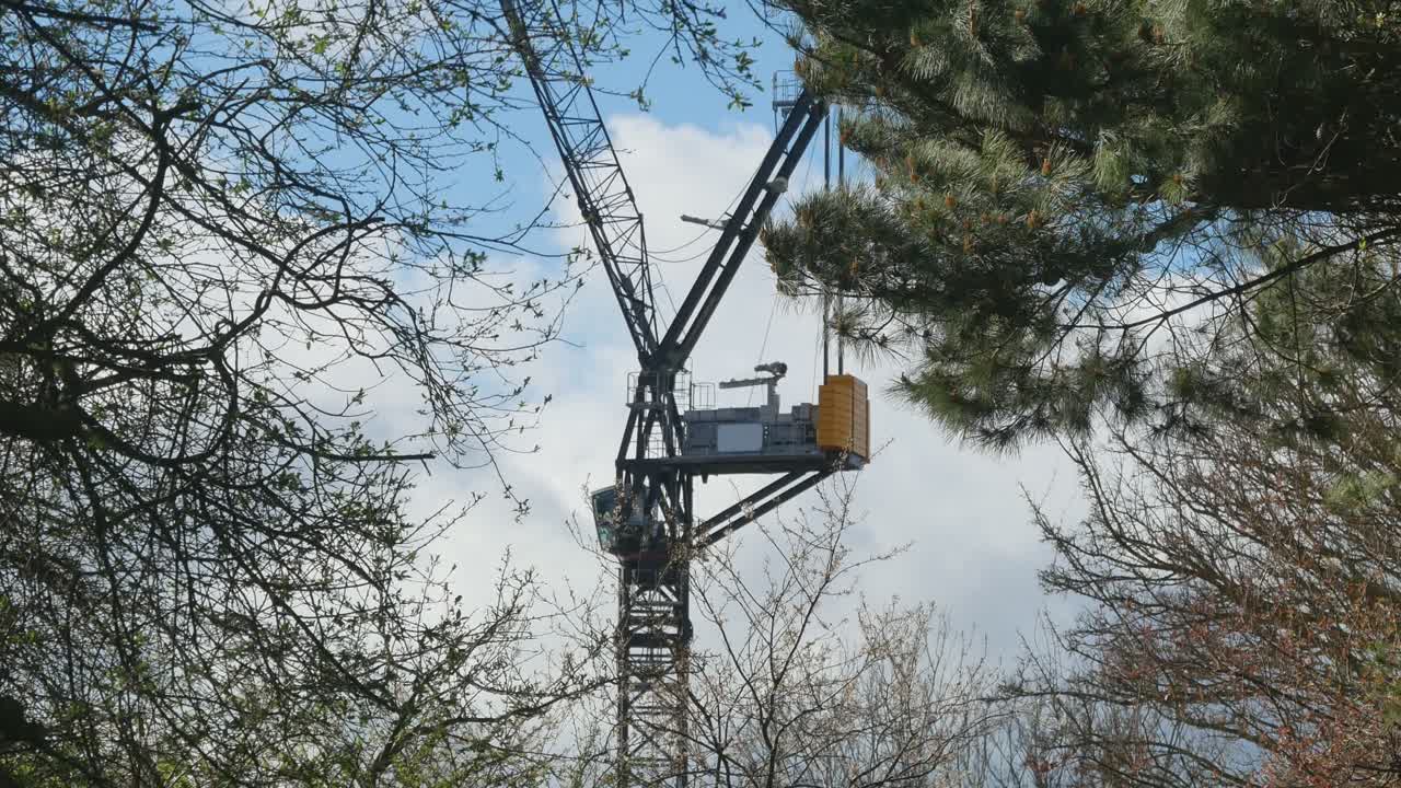 Construction Crane Visible Between Tree Branches On A Sunny Spring Day. 4K Handheld Footage