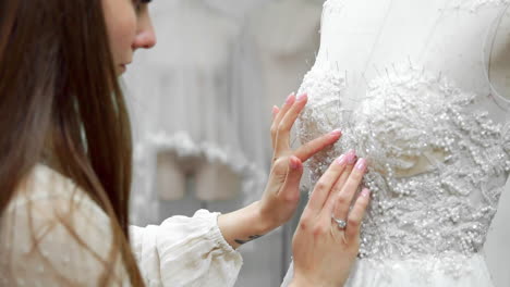 retrato de una chica creando un vestido de novia por pedido exclusivo cosiendo telas y piedras en un vestido vestido con un maniquí. producción de vestidos de novia. pequeño negocio