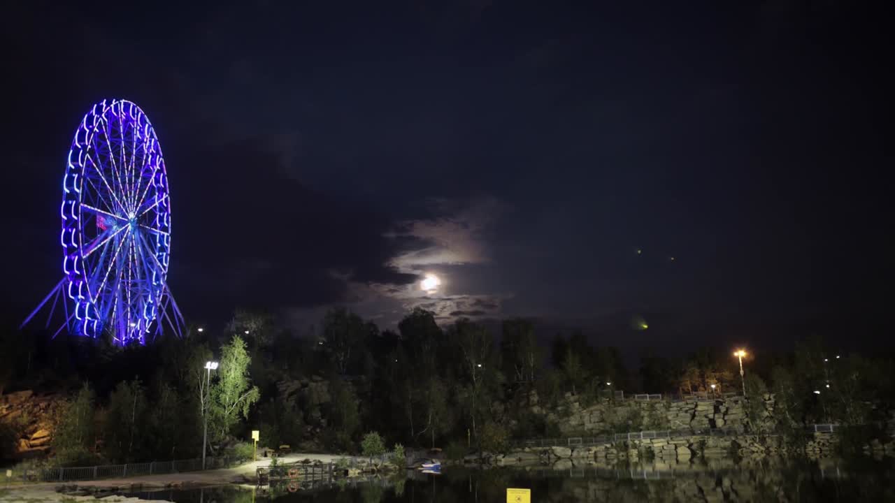 vista nocturna de una rueda gigante con un cielo iluminado por la luna y el paisaje circundante