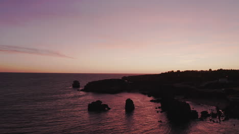 Majestic-aerial-backwards-shot-of-outstanding-rocks-from-the-ocean-and-coastline-after-sunset