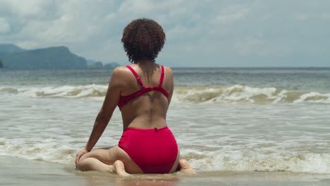 Una-Playa-De-Una-Isla-Tropical-Cobra-Vida-Cuando-Una-Joven-Con-Cabello-Rizado-Se-Arrodilla-En-La-Arena-Con-Un-Bikini-Rojo-En-Un-Día-Soleado