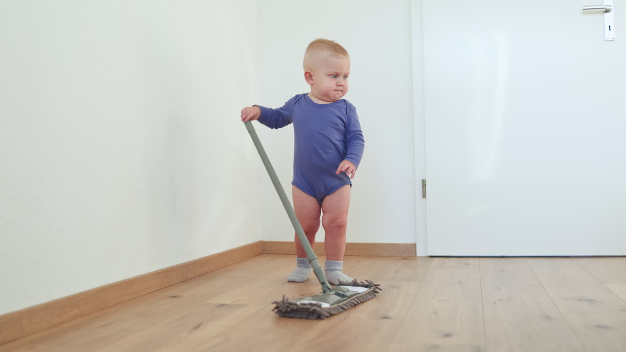 Little boy toddler washes the floor with a mop. Child helps clean the floor. Boy in a cotton bodysuit