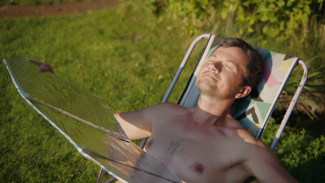 Uomo che si rilassa su una sedia da giardino, usando un fornello solare e bevendo una bevanda calda