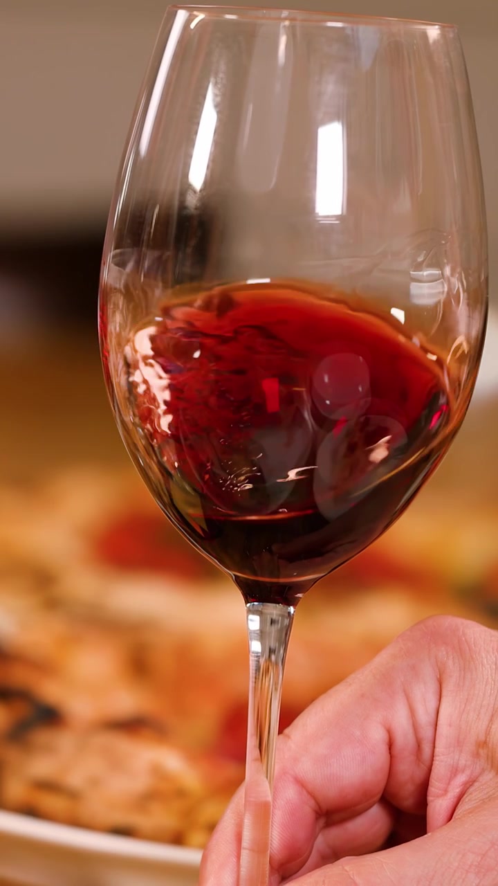 Una persona fa roteare vino rosso in un bicchiere sopra una pizza in un ristorante italiano.