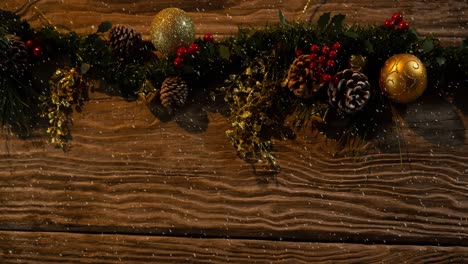 animation of christmas baubles decoration with snow falling on wood