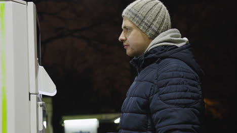 man grabs card from machine and presses to select option and choices in keypad at petrol station on cold night