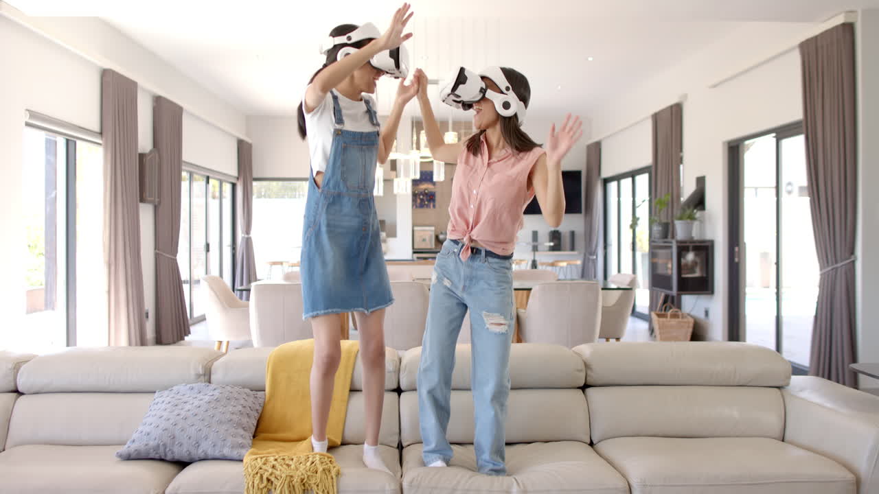 Teenage girls wearing VR headsets, dancing on couch, having fun together